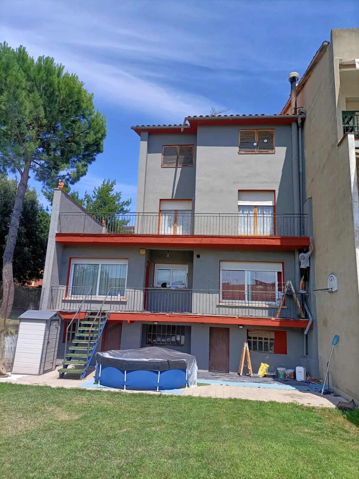 Casa de varias plantas con fachada gris y vuelos rojos recién pintada