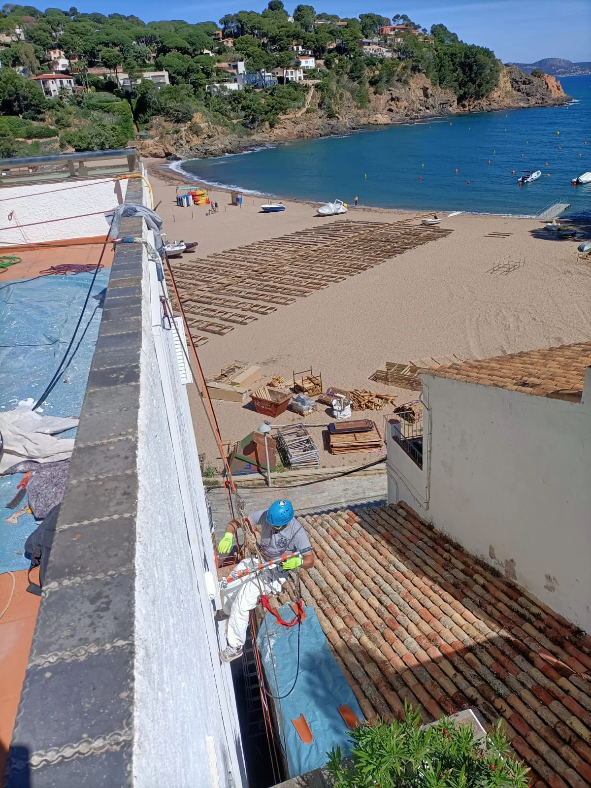 Operario con arneses trabajando en la fachada de un edificio frente a una playa