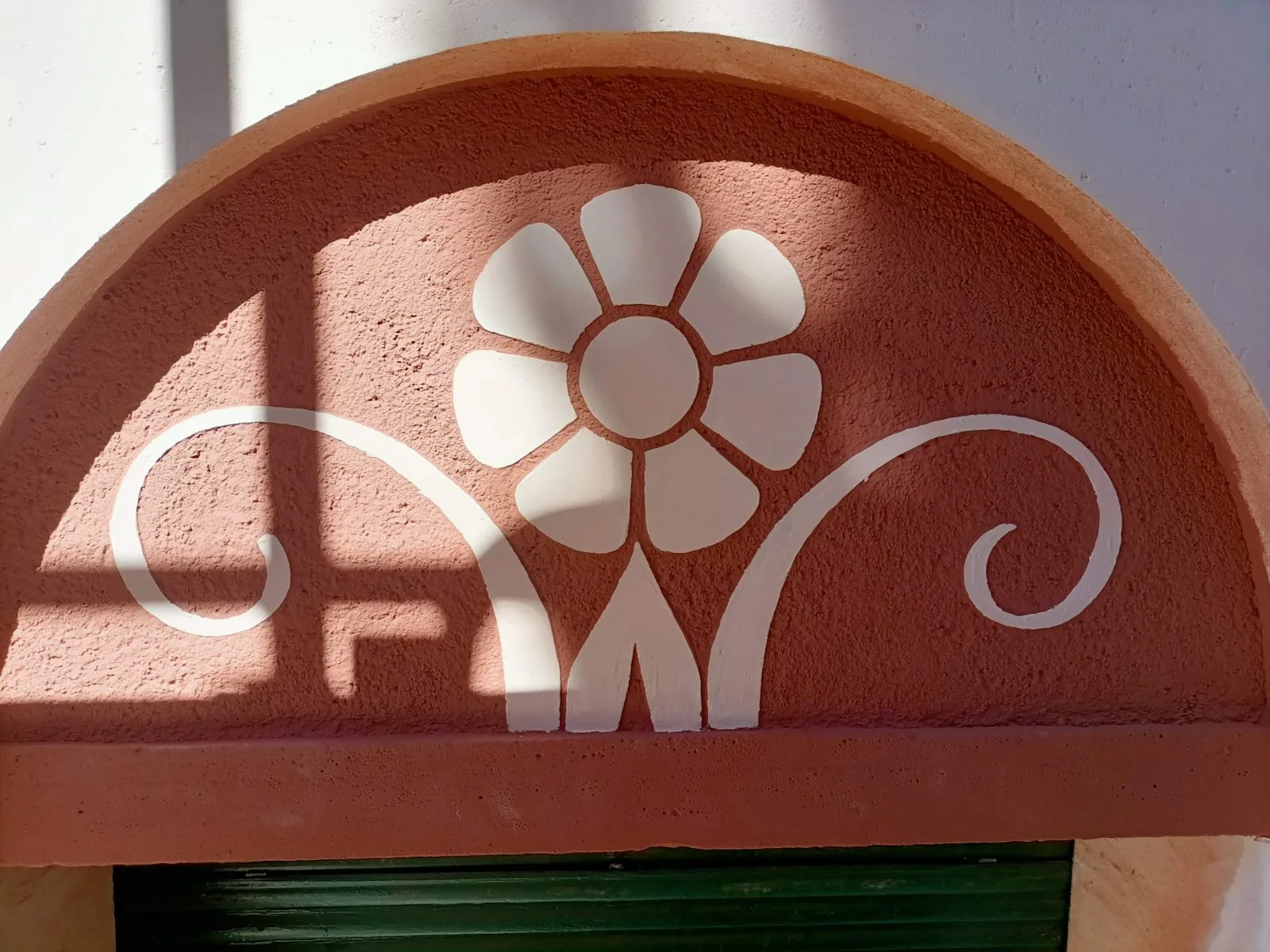 Arco decorativo en fachada con flor y volutas blancas sobre fondo terracota